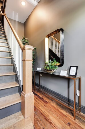 A staircase with wooden steps and a handrail, leading to a landing with a console table, a potted plant, and a mirror.