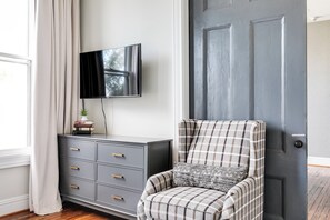 A room with a grey cabinet, a television mounted on the wall, a plaid armchair with a patterned pillow, and a dark grey door. - Modern Luxe Apartment - Close to City Center (Richmond)