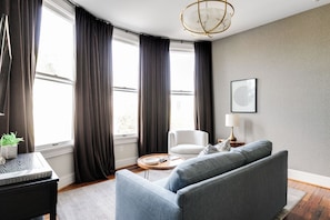 A modern living room with a sofa, a side table, a lamp, and a framed artwork on the wall. - Modern Luxe Apartment - Close to City Center (Richmond)