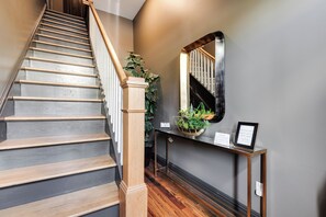 A staircase with wooden steps and a handrail, leading to a landing with a console table and a mirror. - Modern Luxe Apartment - Close to City Center (Richmond)