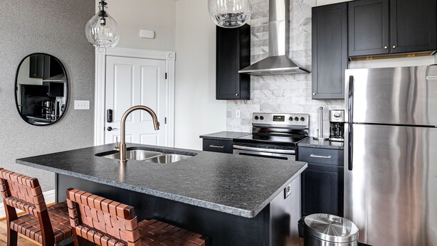 A modern kitchen with a central island, stainless steel appliances, and black cabinetry. - Modern Luxe Apartment - Close to City Center (Richmond)