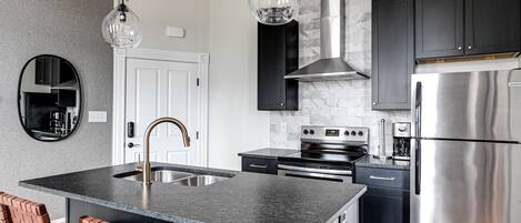 A modern kitchen with a central island, stainless steel appliances, and a black and white marble backsplash.