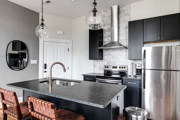 A modern kitchen with a central island, stainless steel appliances, and black cabinetry. - Modern Luxe Apartment - Close to City Center (Richmond)