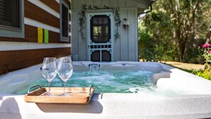 Een hottub met twee glazen en een dienblad, een houten hutje met een deur versierd met groen, en een tuin met bomen en bloemen.