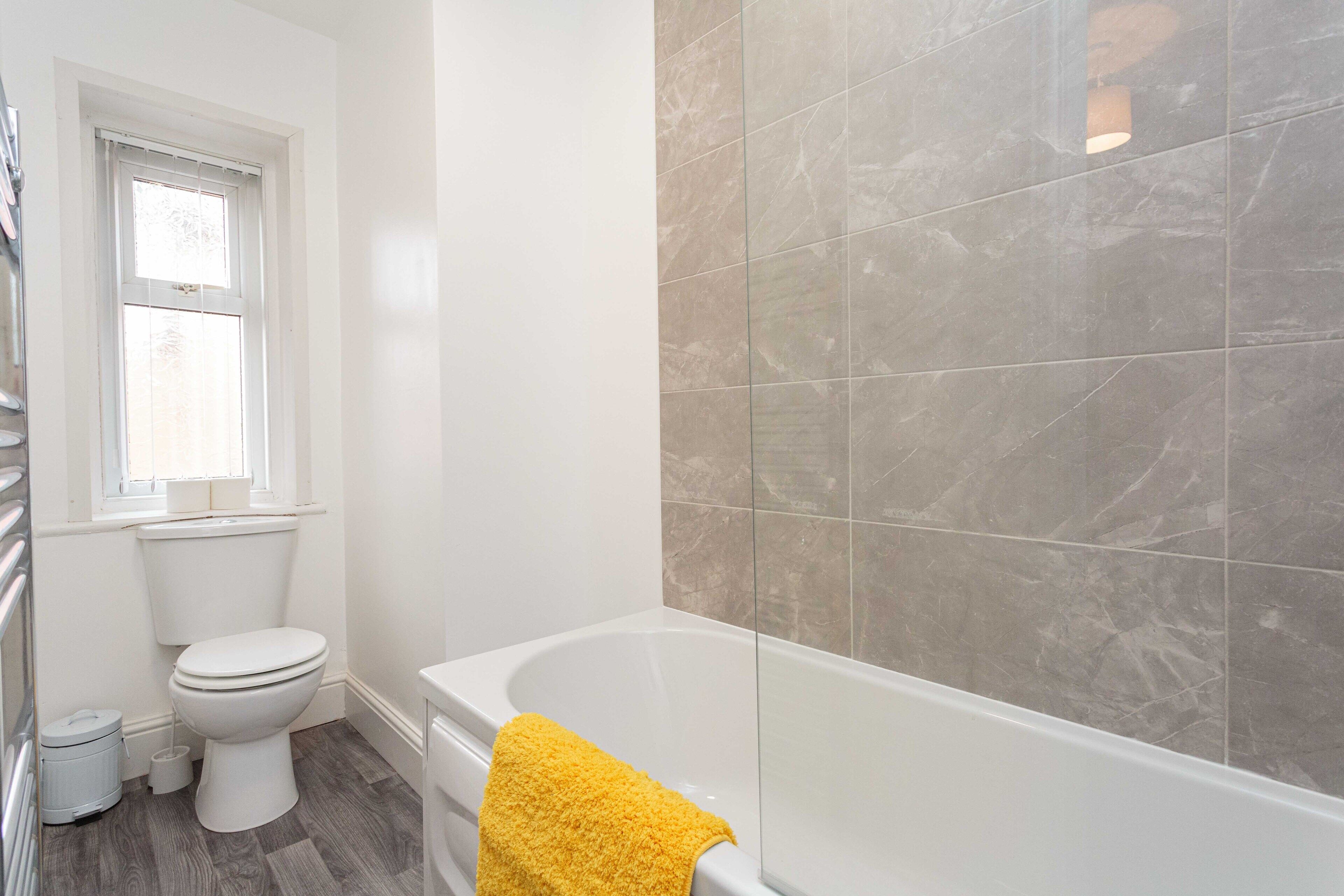 A bathroom with a toilet, a bathtub, and a window.