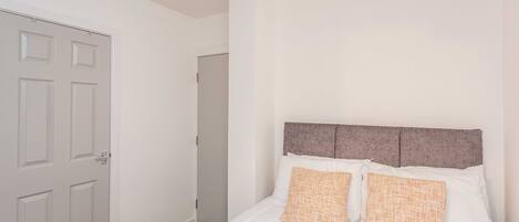 A bedroom with a bed, two pillows, a headboard, and a door.