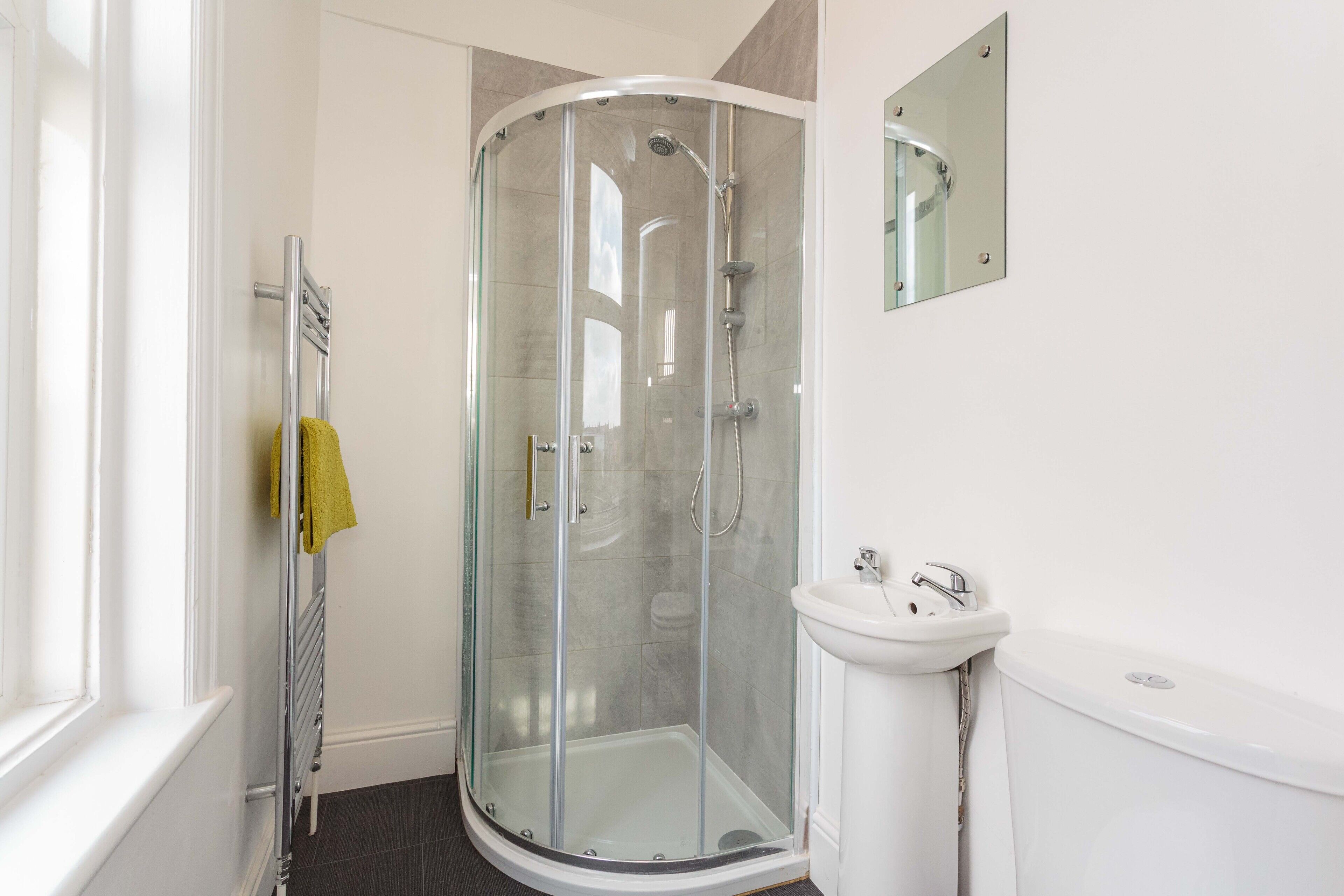 A modern bathroom with a glass-enclosed shower, a white sink, and a mirror above the sink.
