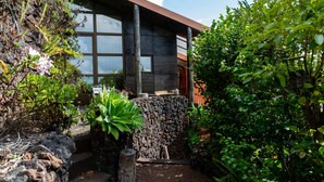 A modern building with large windows, a stone wall, and lush greenery. - Caloura 66 - Vacation Villa (Lagoa)