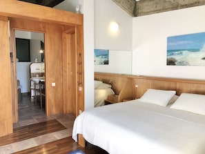Een slaapkamer met een houten hoofdbord, een bed met wit beddengoed, een nachtkastje met een lamp, en een schilderij van de oceaan aan de muur.