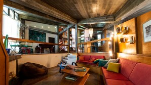 A cozy interior with a wooden ceiling, a red sofa, a wooden coffee table, and a staircase leading to an upper level. - Caloura 66 - Vacation Villa (Lagoa)