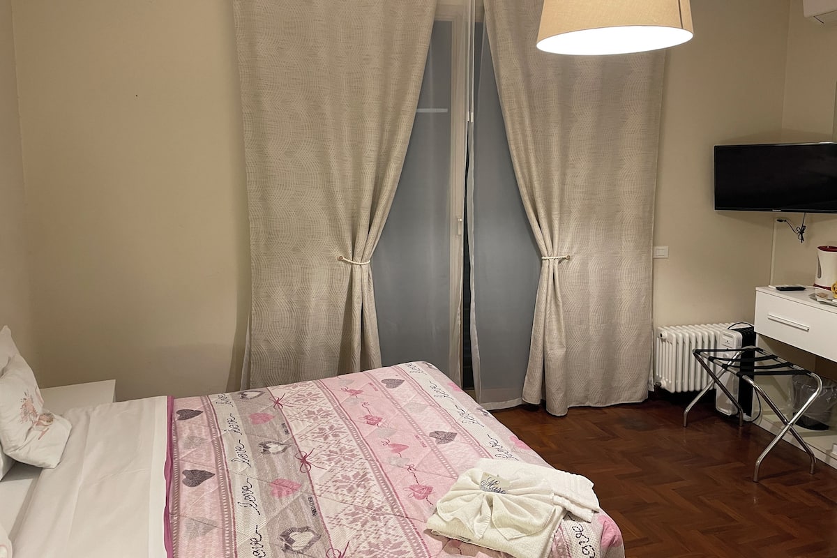 A bedroom with a bed, a TV, a radiator, and curtains.