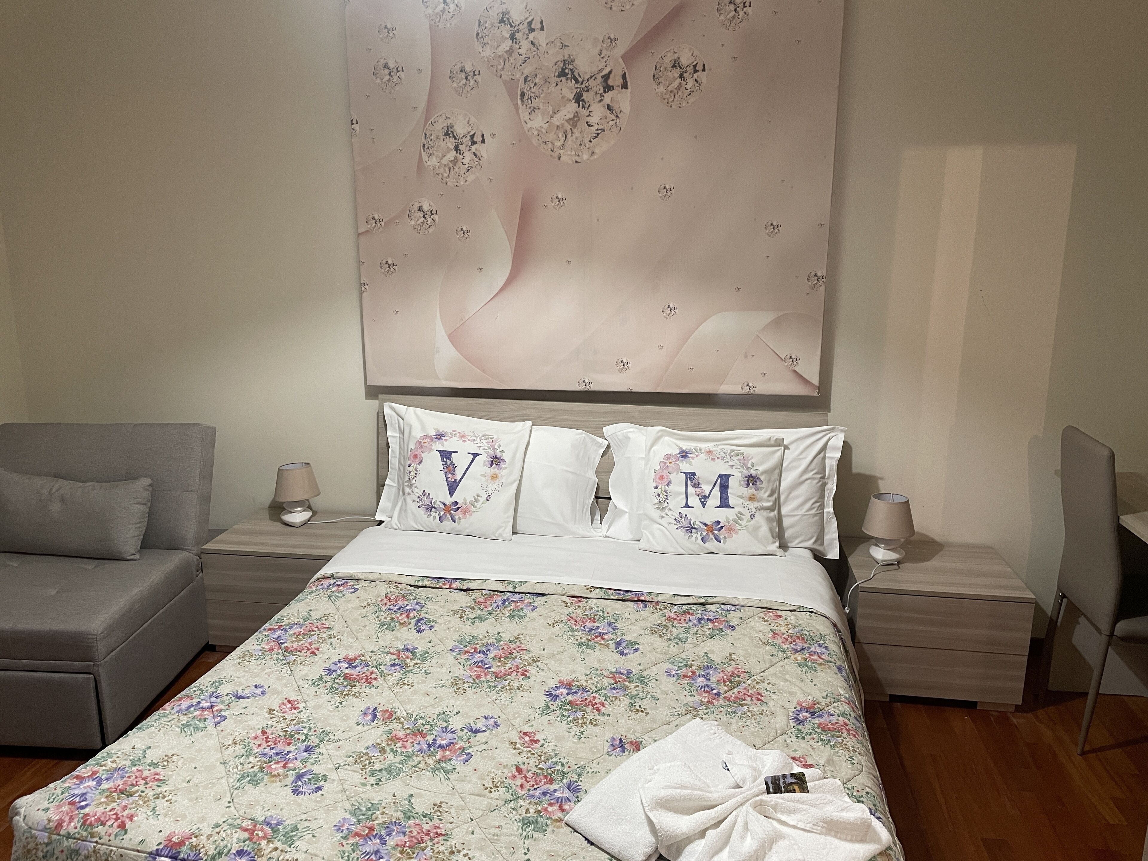 Un dormitorio con colcha estampada, un sofá gris y una mesita de noche con lámpara.