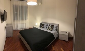 Un dormitorio ordenado con cama, mesitas de noche, una lámpara y un televisor.