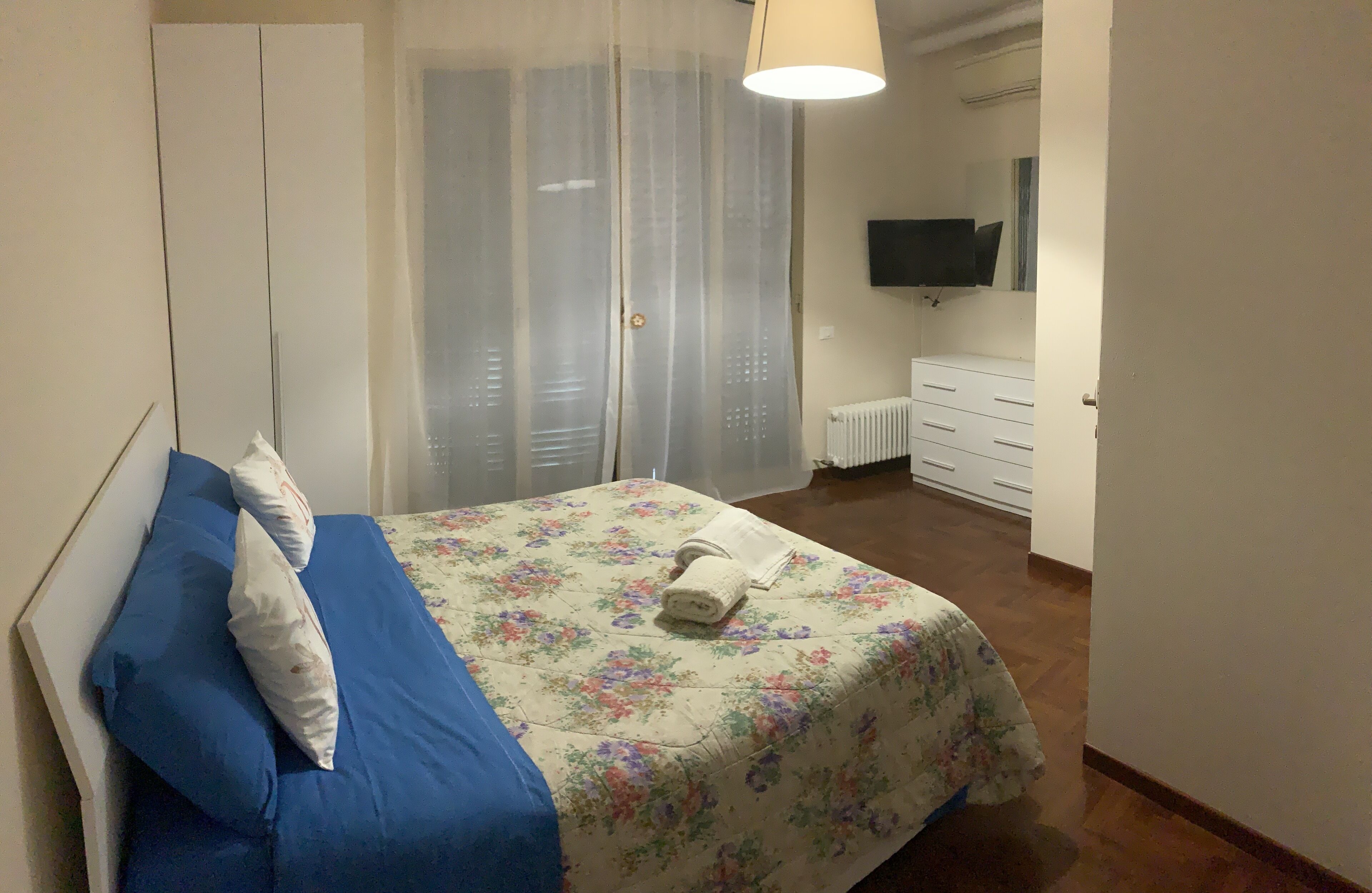 A bedroom with a bed, a wardrobe, a radiator, and a television on the wall.
