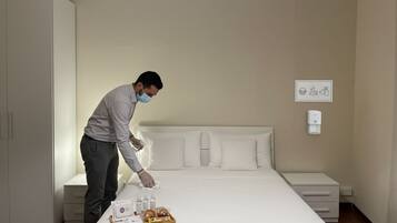 Una camera d'albergo con un letto rifatto, un comodino con una lampada, uno scolaretto e un armadio.
