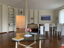 Una sala de estar con una mesa de vidrio, un sofá, un comedor con sillas y una estantería.