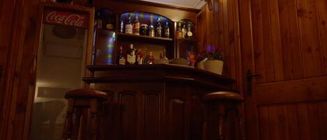 A bar area with wooden cabinets, shelves with liquor bottles, and a Coca-Cola refrigerator.