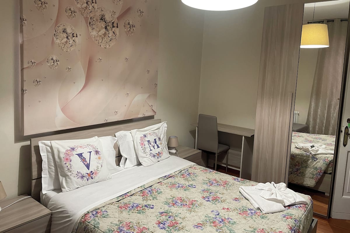 A hotel room with a bed, a desk, and a mirror.