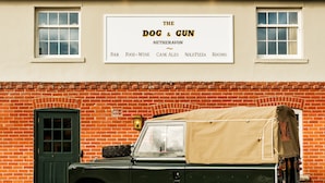 Un edificio con un letrero que dice "The Dog & Gun" y un vehículo verde estacionado en la parte delantera.