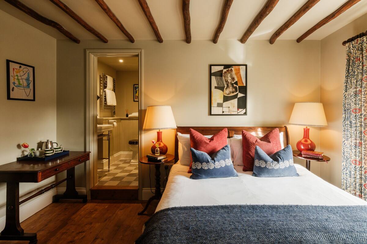 A hotel room with a large bed, wooden beams on the ceiling, two bedside lamps, and a checkered floor.