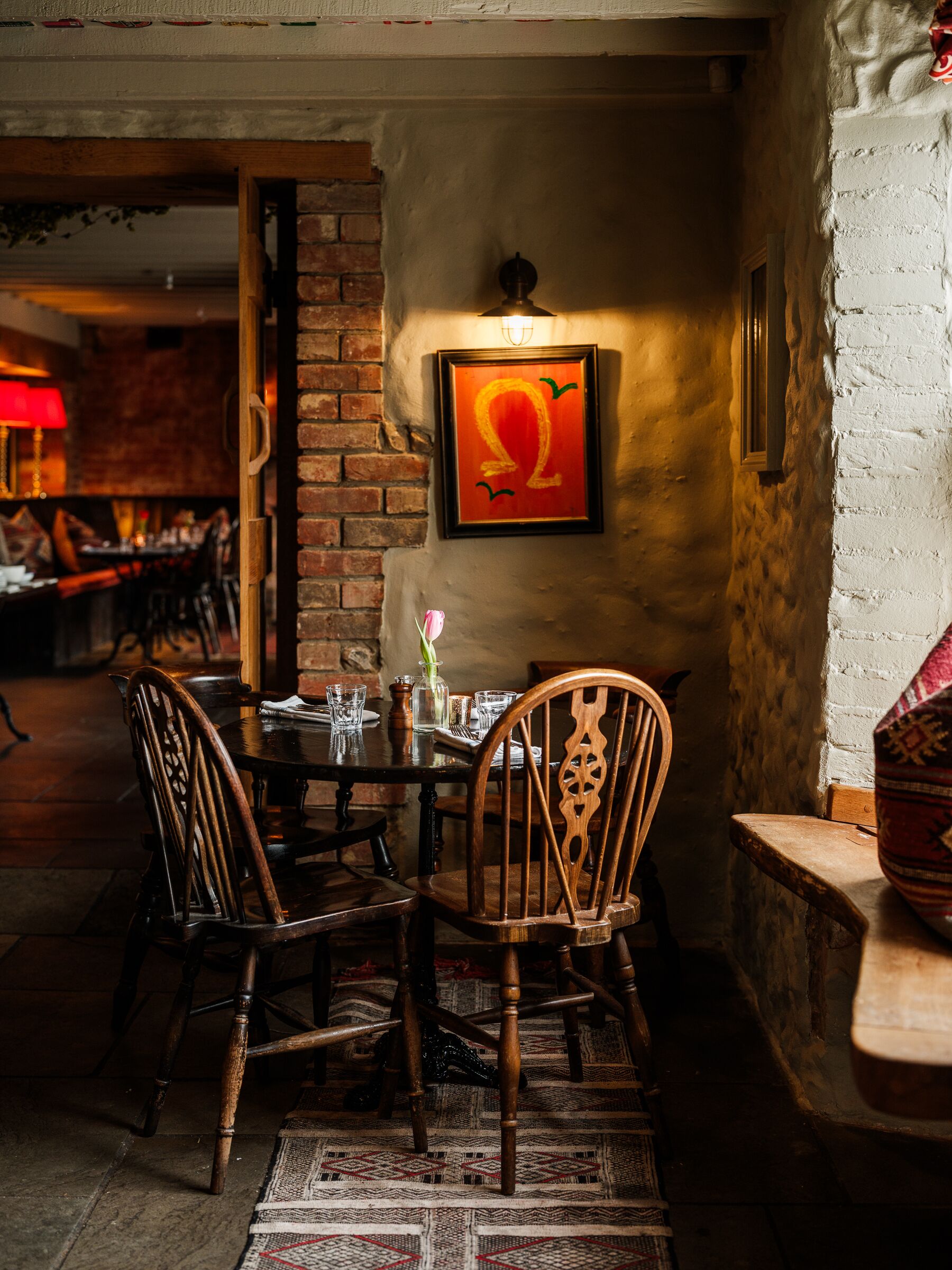 A cozy dining area with a brick wall, wooden chairs, a round table, and a framed artwork.