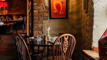 A cozy dining area with a brick wall, wooden chairs, a round table, and a framed artwork.
