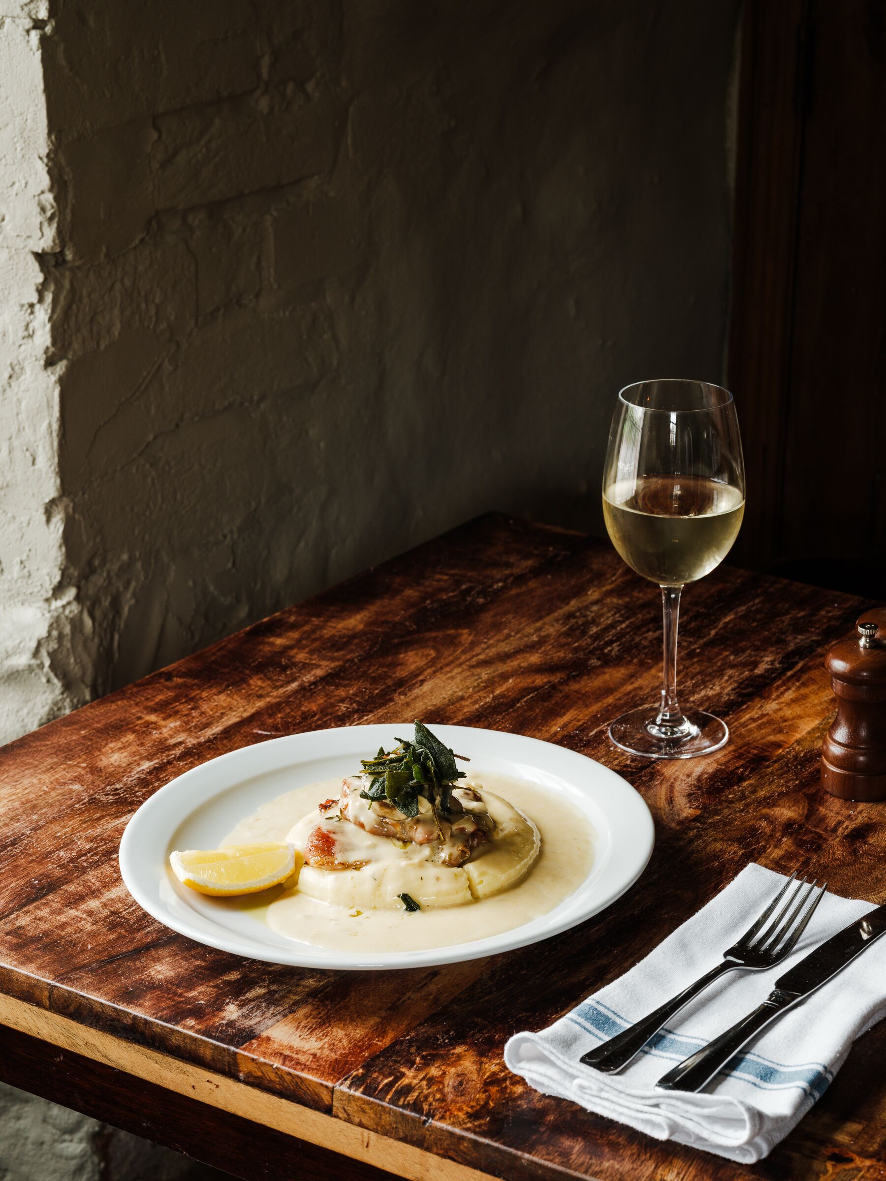 Una mesa de madera con un plato de comida y una copa de vino blanco.