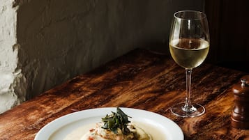 Una mesa de madera con un plato de comida y una copa de vino blanco.