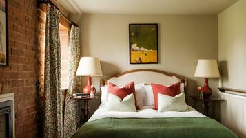Un dormitorio ordenado con pared de ladrillo, cortinas florales, un cuadro y dos mesitas de noche con lámparas.