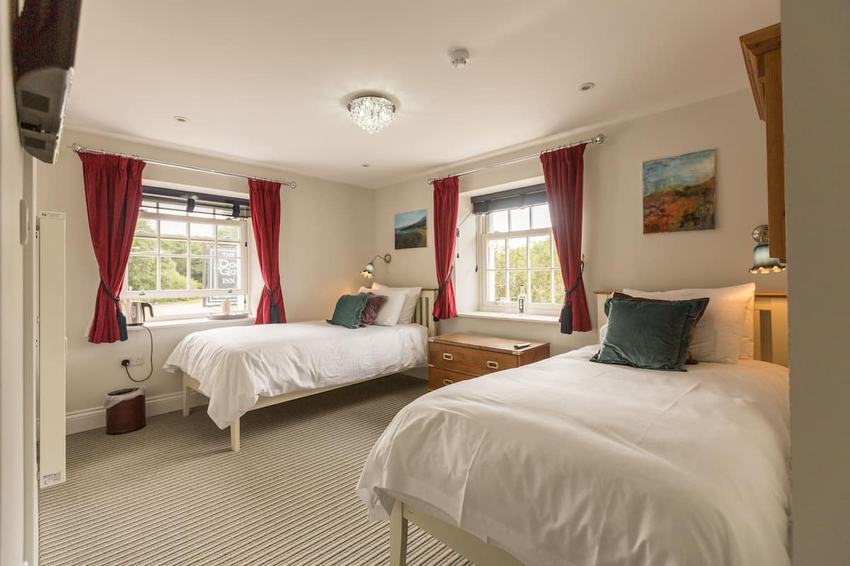 A bedroom with two beds, a nightstand, a lamp, and a window with curtains.