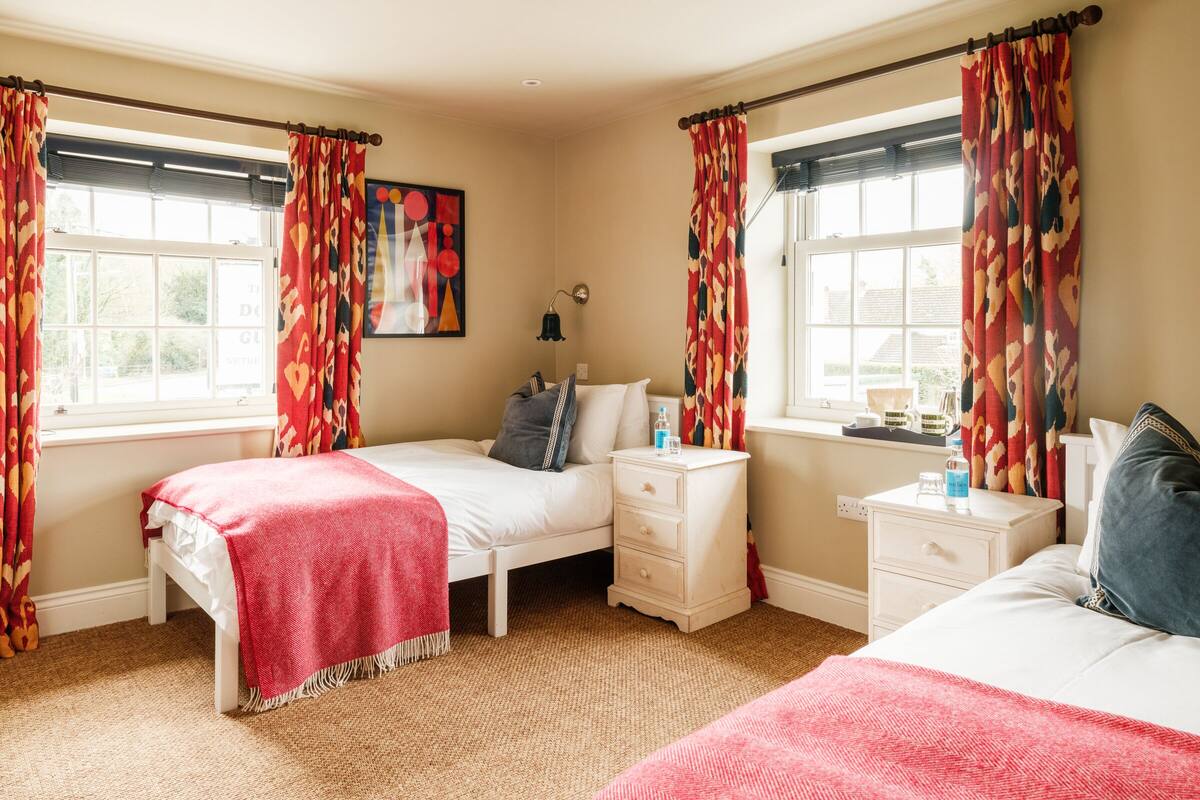 A bedroom with two beds, a bedside table with a lamp, and a window with curtains.