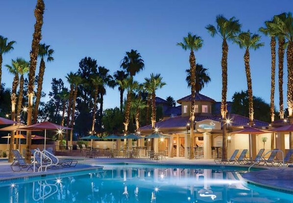 Relax by the resort pool surrounded by palm trees and lounge chairs.