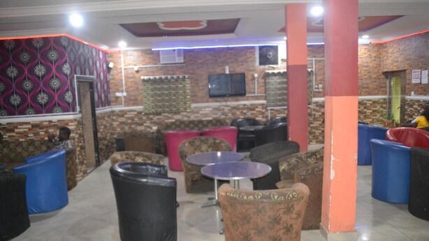A lounge area with patterned walls, a TV mounted on the wall, and various seating options including sofas and chairs. - Evaville Hotel N Lounge (Port Harcourt)