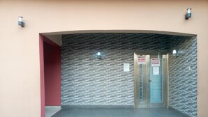 A building entrance with a stone-patterned wall, a red pillar, and a set of double doors with signs indicating no guns or alcohol allowed. - Evaville Hotel N Lounge (Port Harcourt)