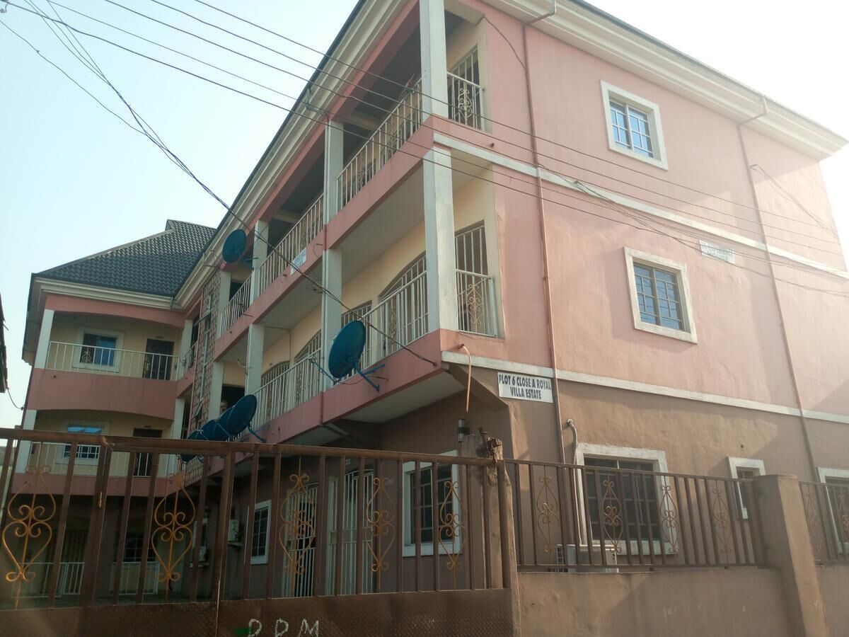 A multi-story pink building with balconies, a gated entrance, and a satellite dish.
