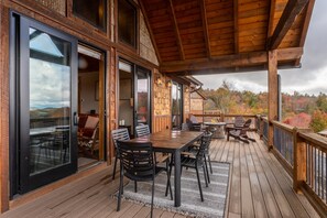 Enjoy a comfortable seating area with a large table, chairs, and a sofa on the deck, offering a view of the surrounding trees.