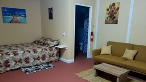 A bedroom with a bed, a sofa, a coffee table, and a bathroom visible through an open door.
