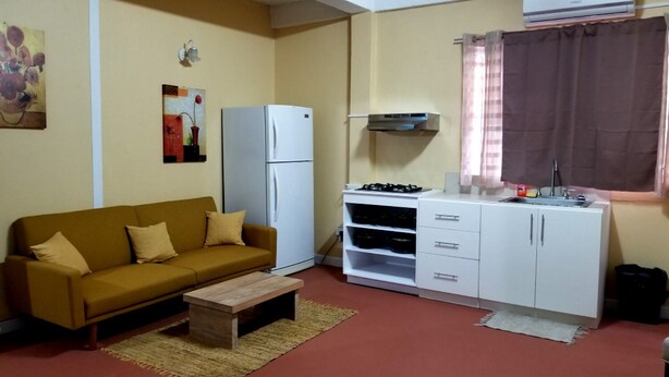 A compact living space with a sofa, a small table, a kitchenette with a stove, and a refrigerator.
