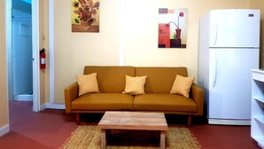 A living room with a sofa, a coffee table, a refrigerator, and two wall-mounted paintings.