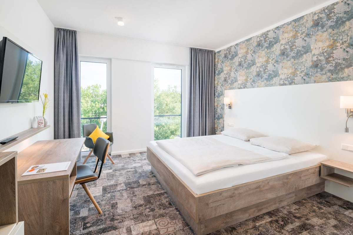 A modern hotel room with a large bed, a desk, a chair, and a TV.