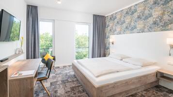 A modern hotel room with a large bed, a desk, a chair, and a TV.