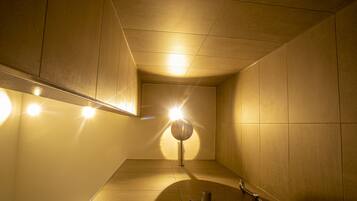 Une salle de bain moderne et bien éclairée, avec un grand miroir rond, des toilettes et un lavabo.