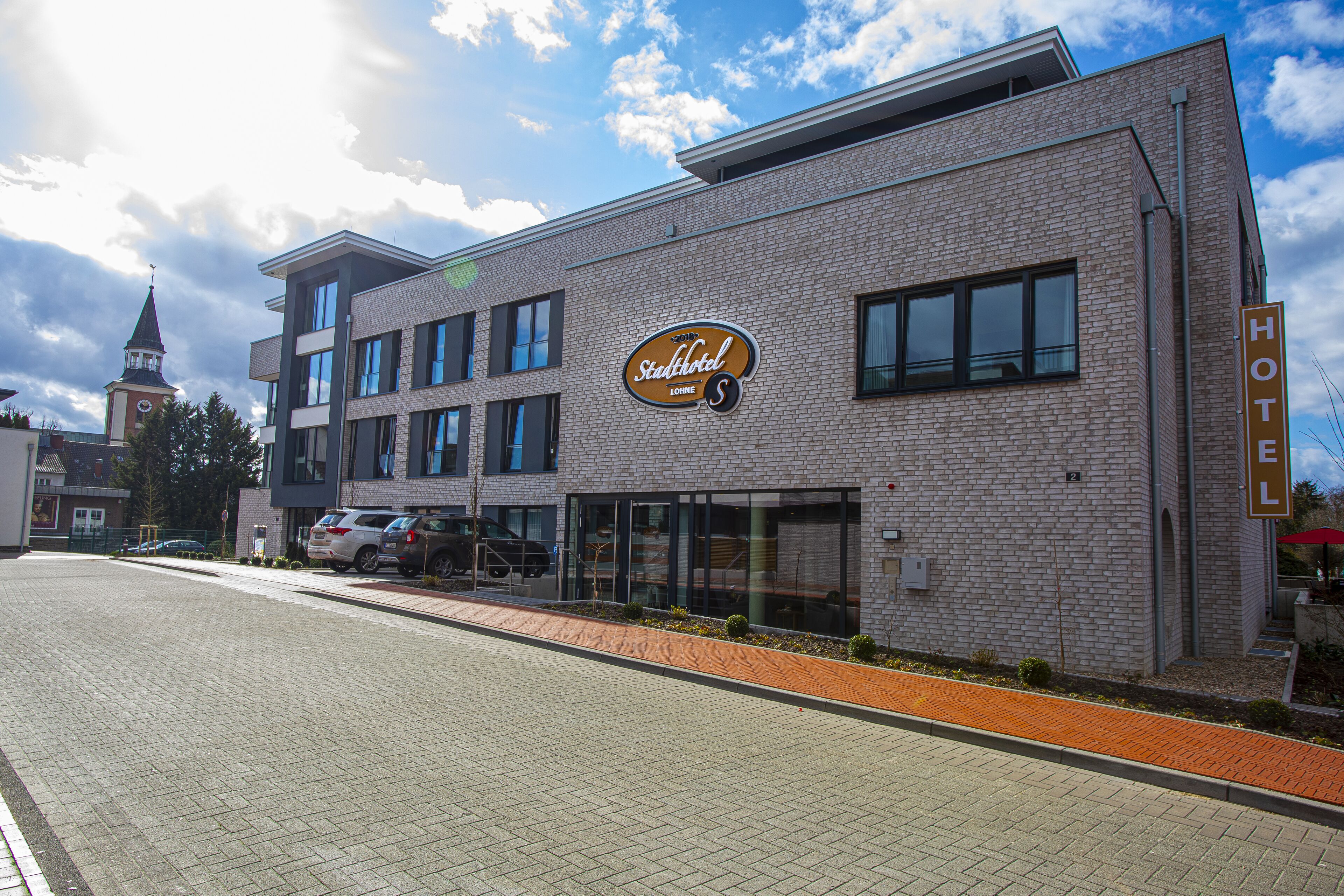 A hotel with a modern brick facade, a prominent sign, and a visible clock tower in the background.