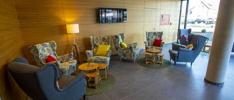 A modern lobby with patterned armchairs, a sofa, and a television mounted on the wall.
