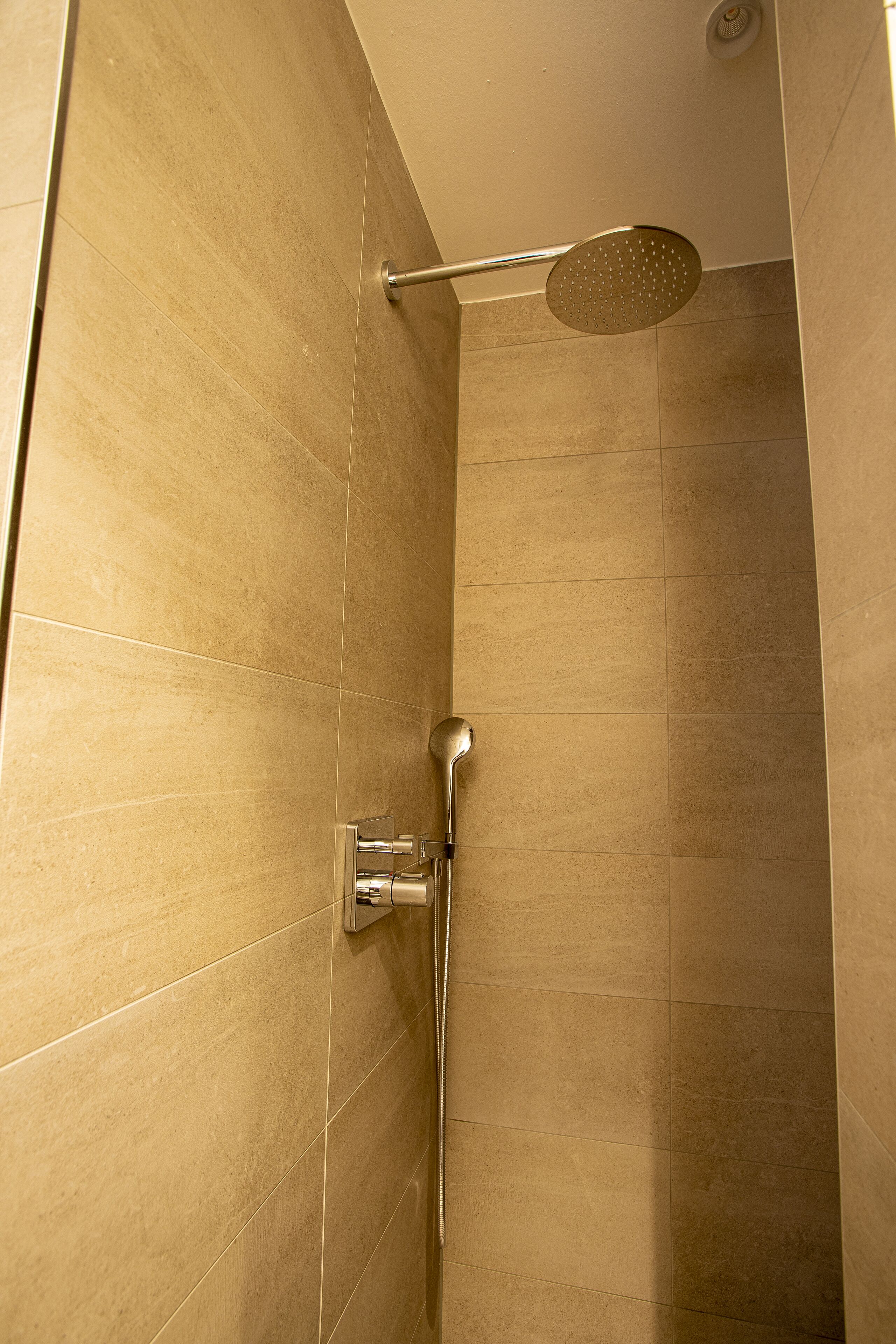 A shower with a handheld showerhead and a wall-mounted control panel.