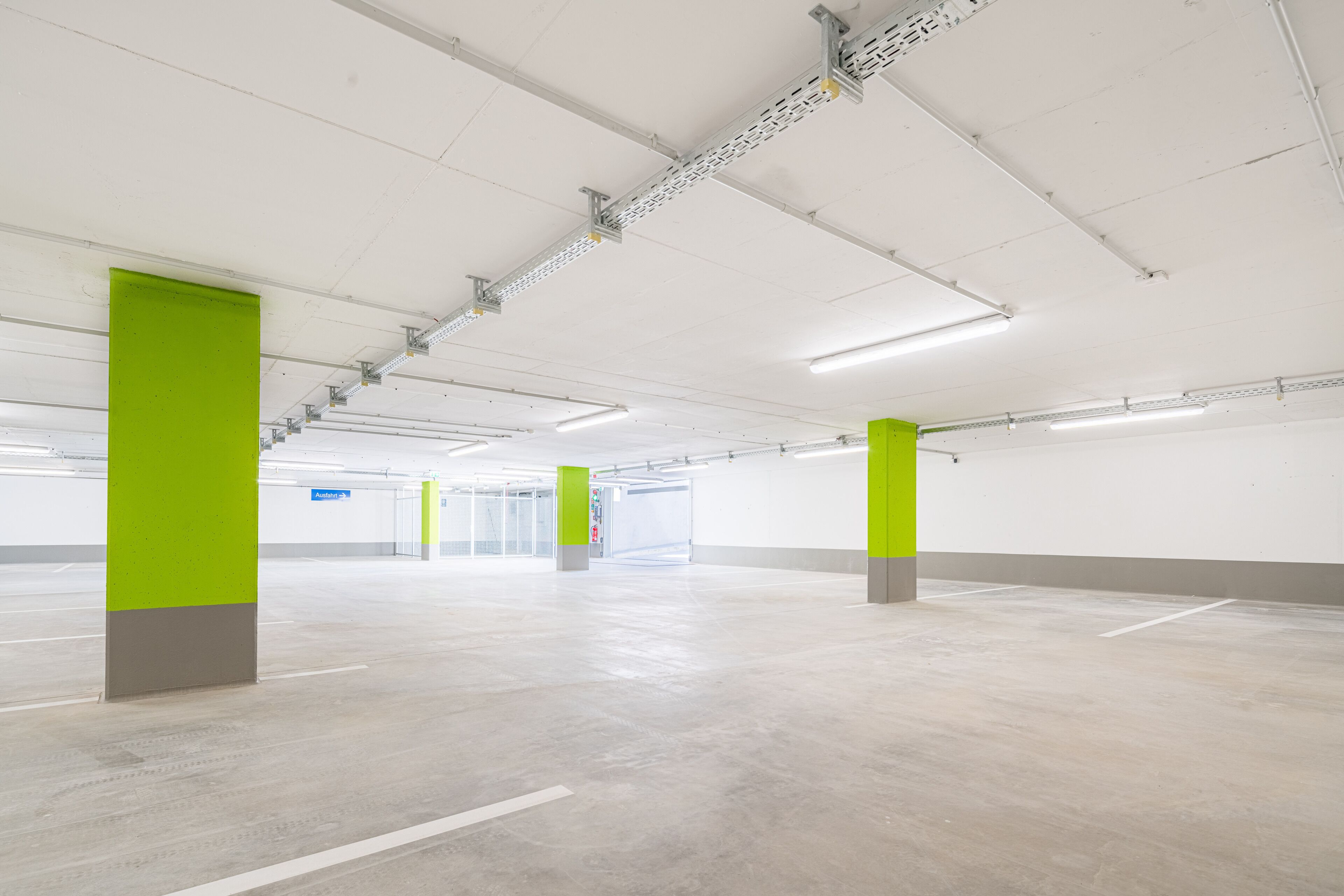 Amplo espaço de estacionamento interno, com iluminação brilhante e pilares verdes.