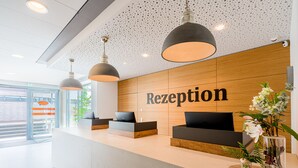 A reception area with a wooden wall, a reception desk, and two black sofas.