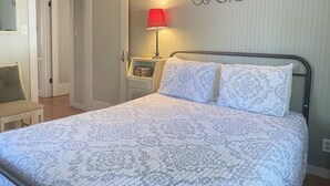 A neatly made bed with patterned bedding, a bedside table with a lamp, and a chair. - Lago Haus, Top Unit, Rustic Wundercove Cottage, Access to Shared Pool and River (New Braunfels)