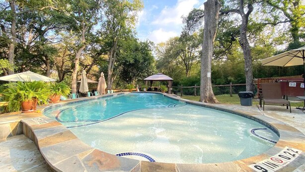 A swimming pool with a stone border, surrounded by trees and outdoor furniture. - Lago Haus, Top Unit, Rustic Wundercove Cottage, Access to Shared Pool and River (New Braunfels)