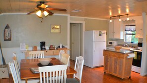 A kitchen with a wooden table, chairs, a refrigerator, a microwave, and a ceiling fan. - Lago Haus, Top Unit, Rustic Wundercove Cottage, Access to Shared Pool and River (New Braunfels)